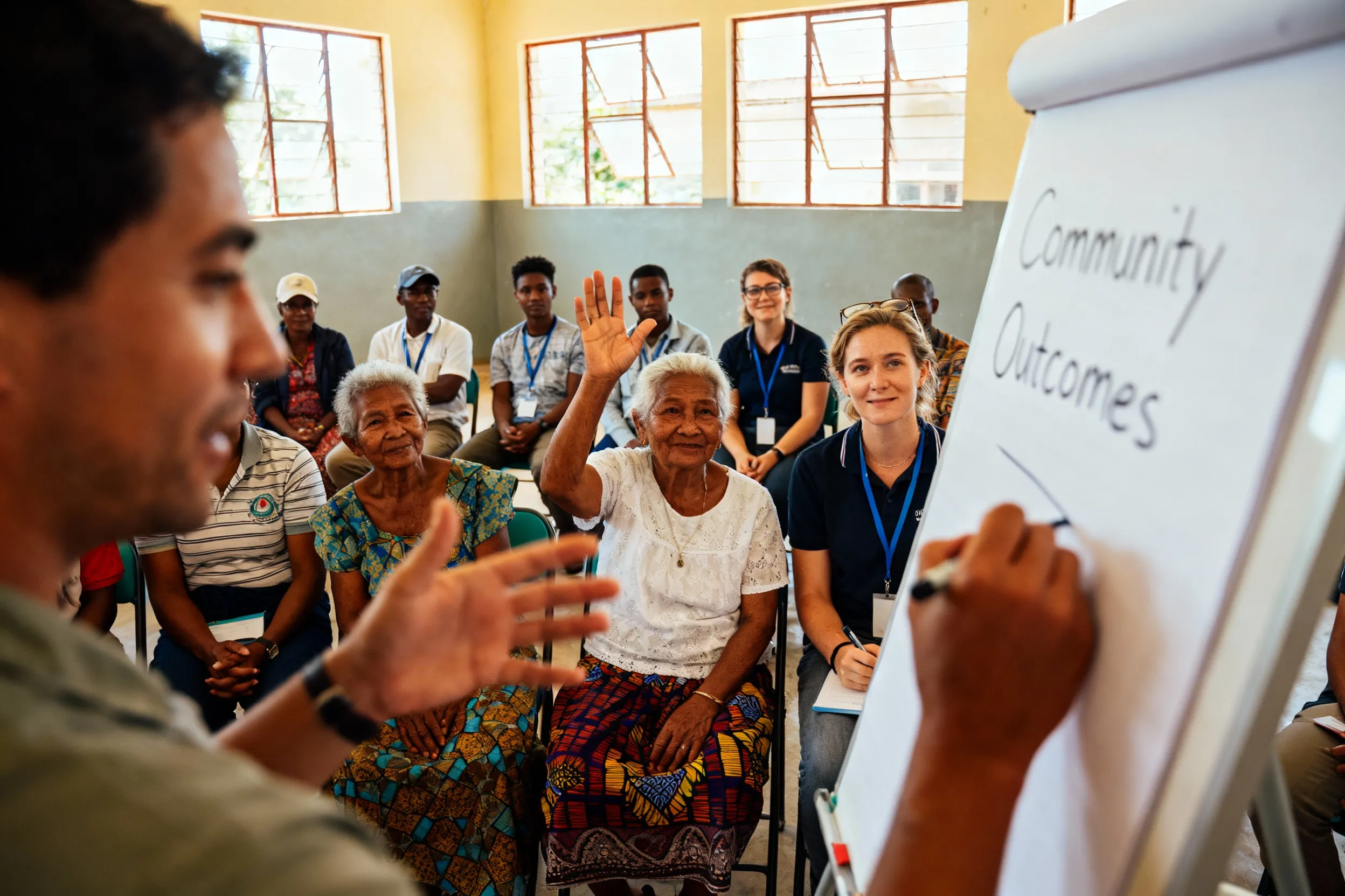 Diverse community participants engaged in outcome harvesting workshop with flipcharts, demonstrating participatory monitoring and evaluation methodology